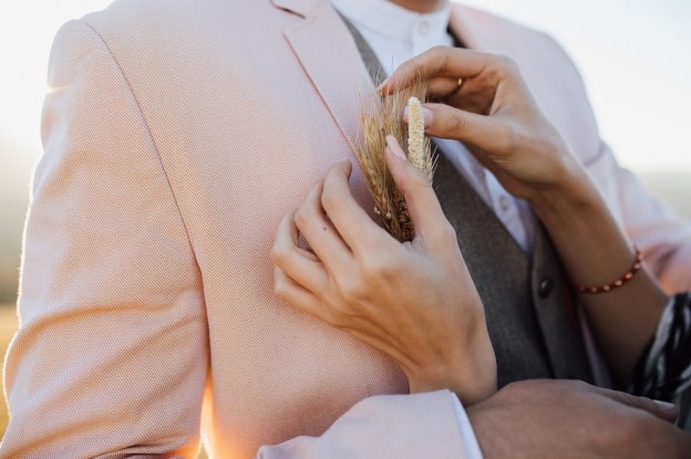 A woman is fixing a stylish bridal wheat buttonhole to a man